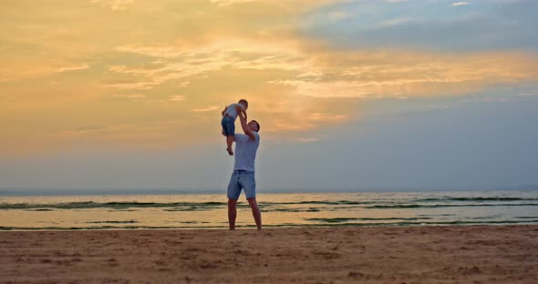 Young Loving Dad Plays with His Little Son on the Seashore Throws the Child Up