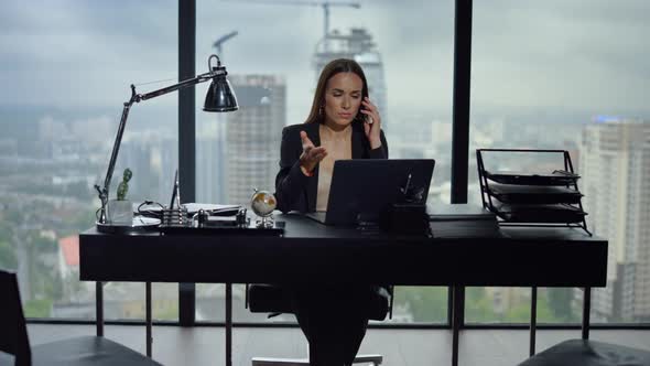 Businesswoman Talking on Smartphone in Office. Woman Looking at Screen of Laptop alt