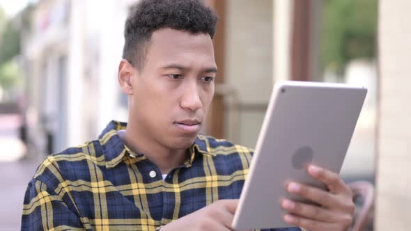 Young African Man Reacting to Loss on Tablet Outdoor alt