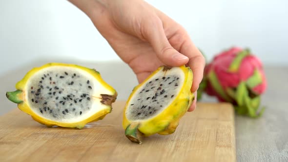 Female Hands is Cutting a Dragon Fruit or Pitaya with Yellow Skin and White Pulp with Black Seeds on alt