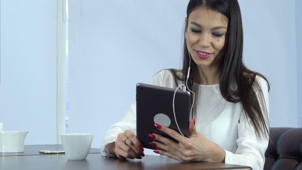 Smiling Woman in Earphones Having Video Call Via Digital Tablet in a Cafe alt