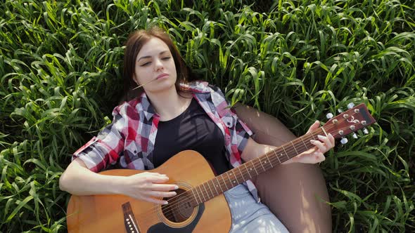 Woman Lies in a Wheat Field Plays Music on Guitar and Sings in Slow Motion at Sunset alt