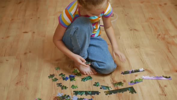 A Beautiful Little Girl Assembles a Complex Puzzle on a Wooden Floor
