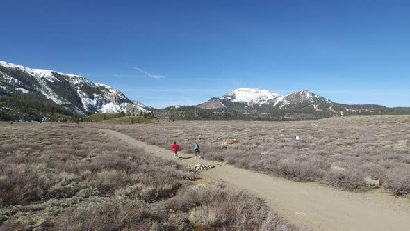 Aerial shot of a young man and woman trail running with dog on scenic mountain trail. alt