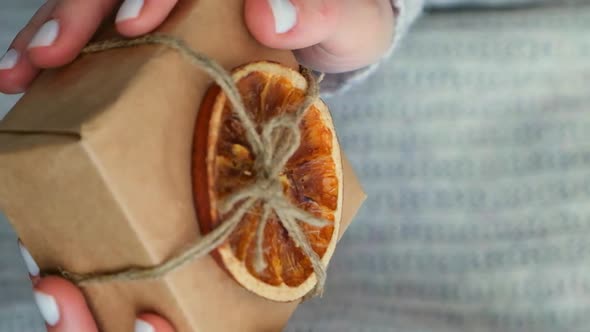Woman Giving Box with New Year's Gifts Wrapped in Craft Paper and Decorated with Dry Orange Slices alt