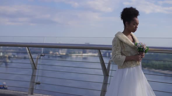 Frustrated Beautiful African American Woman in Wedding Dress Putting Bridal Bouquet on Bridge alt