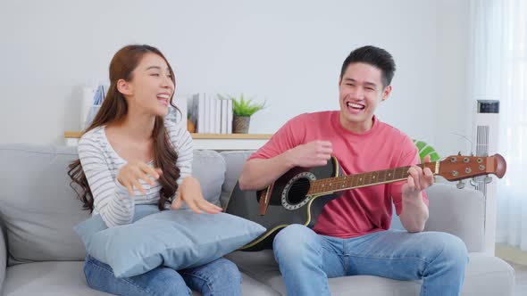 Asian young loving couple play guitar together in living room at home. alt