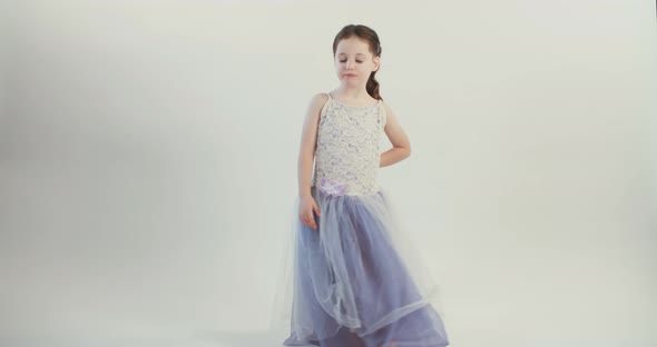 Little girl wearing a dress dances on a white studio background alt