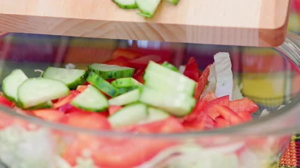 Caucasian Woman Adding Chopped Cucumber Into Glass Bowl with Cut Chinese Cabbage and Red Bell Pepper