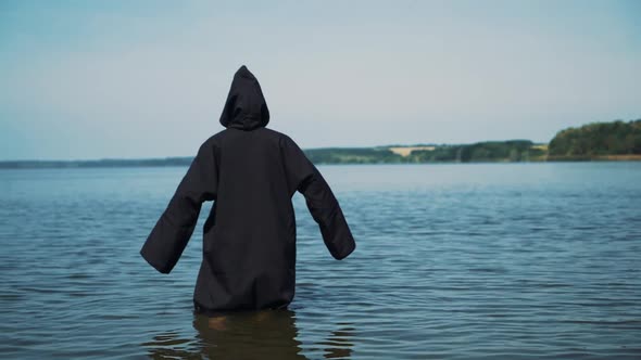Scary figure in black mantle in the river. Mysticism of Halloween. Halloween costume. alt