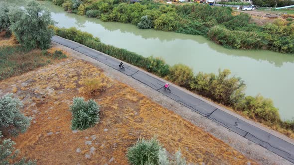 Couple riding bicycles along a trail by a river together - aerial tracking view alt