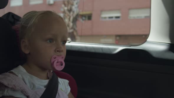 Toddler girl with pacifier traveling by car. Safe ride in child seat alt