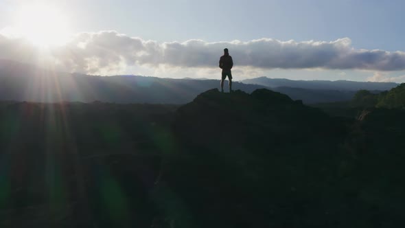 A Man Standing on a Mountain Peak in Rays of Evening Sun alt