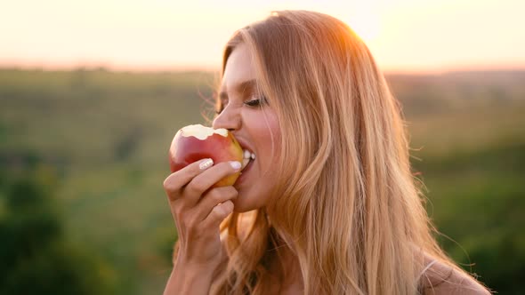 Beautiful sexy blonde girl in white dress posing in a field at sunset with a basket of fruit alt