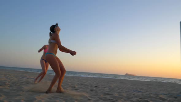 Women players play beach volleyball and a player hitting spiking the ball. alt
