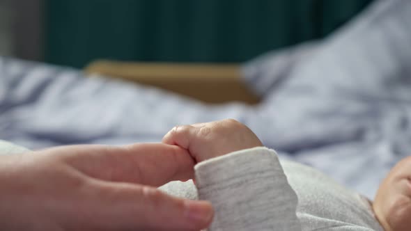 Loving Mother Holds Hand of Newborn Son Lying on Bed alt