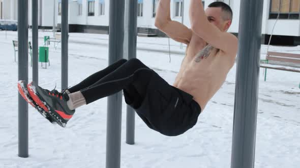 Muscular man training topless on sports field in winter