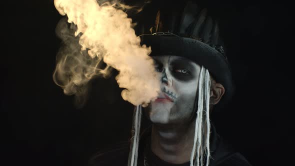 Sinister Man with Professional Skull Makeup Exhaling Cigarette Smoke From His Mouth and Nose alt