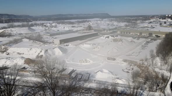 View over large industrial complex with piles of sand covered in snow.  Snow covered river.