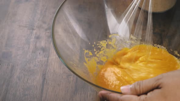 Mixture of egg yolk and sugar being stirred in glass bowl for eggnog cooking