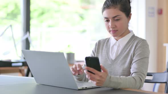 Professional Indian Woman with Laptop Using Smartphone at Work  alt