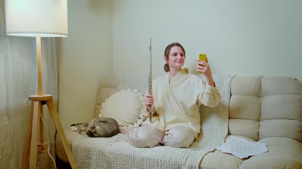 Woman musician with guitar looking at mobile phone at home on sofa in living room
