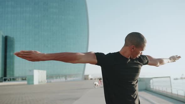 Serious bald sportsman wearing black t-shirt doing hand exercises outdoors alt