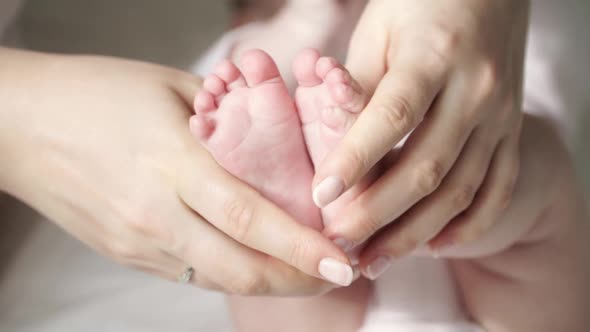 Close up of beautiful young tender mother’s hands hold and caress little cute feet of newborn baby.
