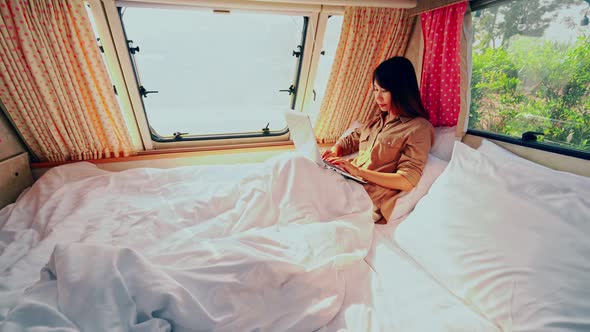 Young woman traveler laying in camper van and using laptop while road trip traveling on vacation