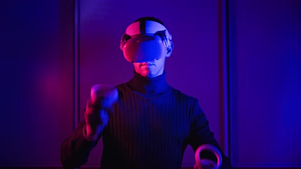 Young Man in VR Helmet Interacts with Virtual Reality Using Controllers alt