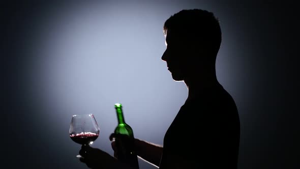 Man Pours Wine Into a Glass and Then Drink It. Back Light alt