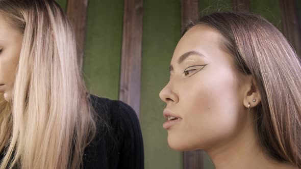 Attractive Caucasian Makeup Artist Doing Makeup for Asian Female in Beauty Salon alt