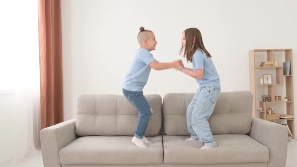 Brother and Sister Play in the Living Room They Jump on the Couch Holding Hands alt