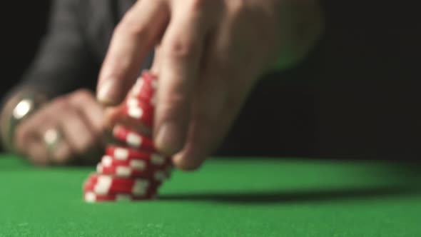 A Close-up of a Male Hand Betting with Red Chips on the Green Poker Table