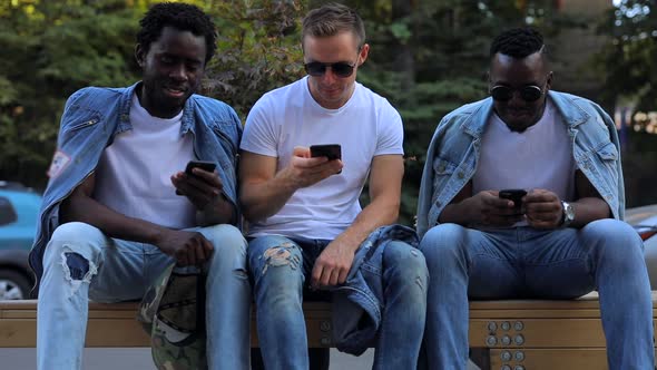 A Multiracial Group of Friends on a Bench Talking and Looking at the Phone alt