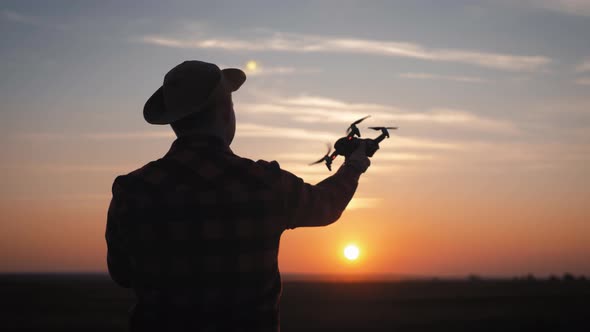 Silhouette of a Farmer Using a Drone in a Wheat Field at Sunset. Concept Technology Innovations for alt