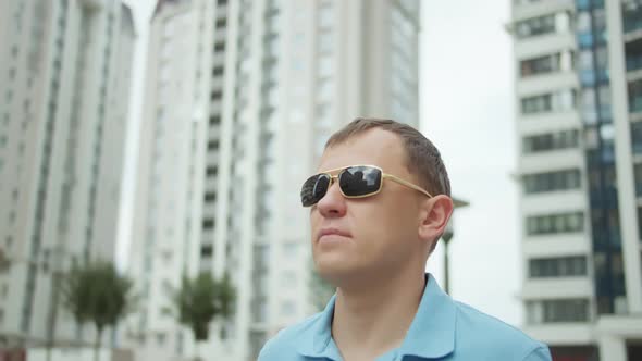 Portrait of a Young Attractive Man on the Background of City Buildings in Sunglasses alt
