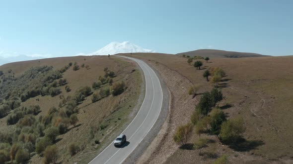 SUV Gray Car Driving in Highland Road on Snowy Mountain Peak Landscape. Automobile Moving on Asphalt alt