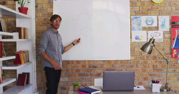 Caucasian male teacher teaching chemistry while looking at laptop in the classroom at school alt