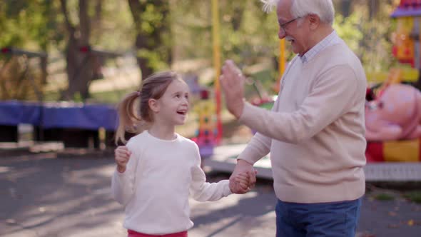 Grandfather having fun with his cute little granddaughter in the amusement park