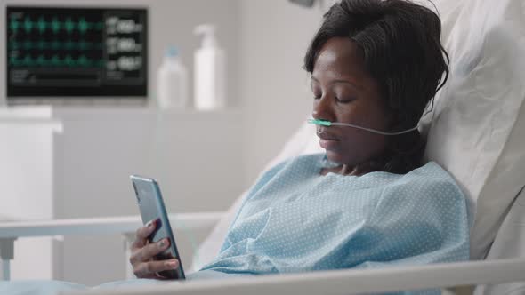A Young Woman Writes a Message on Her Phone While Lying in a Hospital Ward alt