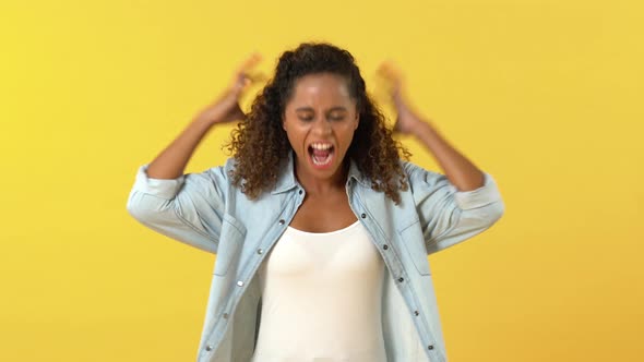 Angry frustrated young African American woman clenching fist and yelling on yellow studio background