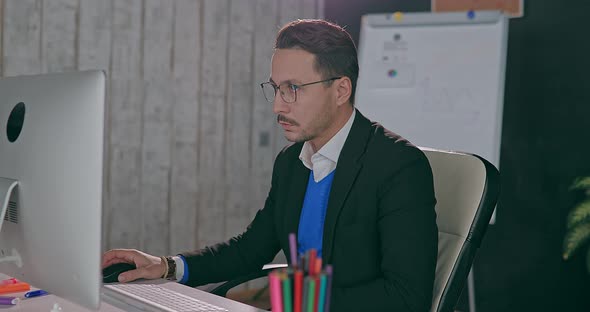 Businessman in Glasses Sits at Computer in Office alt