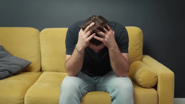 Unshaven Guy Massages His Head on Sofa Suffering From Depression or Headache