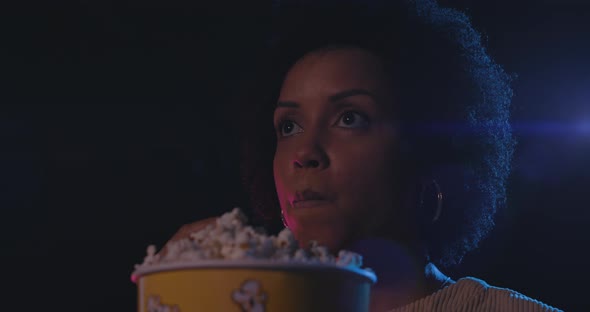 Young  woman watching a movie at the cinema and eating popcorn, entertainment concept