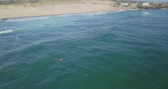 Aerial drone shot flying over surfers on the waves of the atlantic ocean, at sunset, in praia do Gui alt
