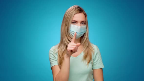 Pretty Woman in Medical Mask Does Disapproving Gesture with Her Finger Against Blue Background alt