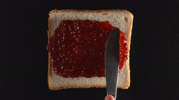 Human hand spreads a raspberry jam on a bread