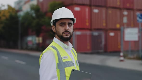 Man in Helmet Holding Tablet While Posing at Cargo Harbor alt