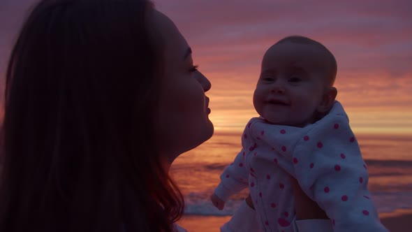 Loving mom hugs her baby at sunset background